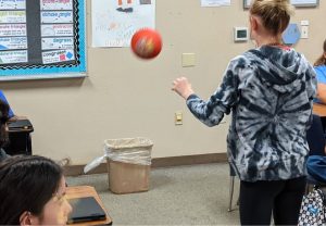 student playing math trashketball using a ball and trash can